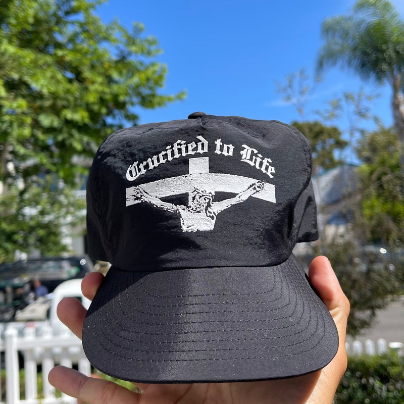 Hand holding the Crucified to Life hat outdoors