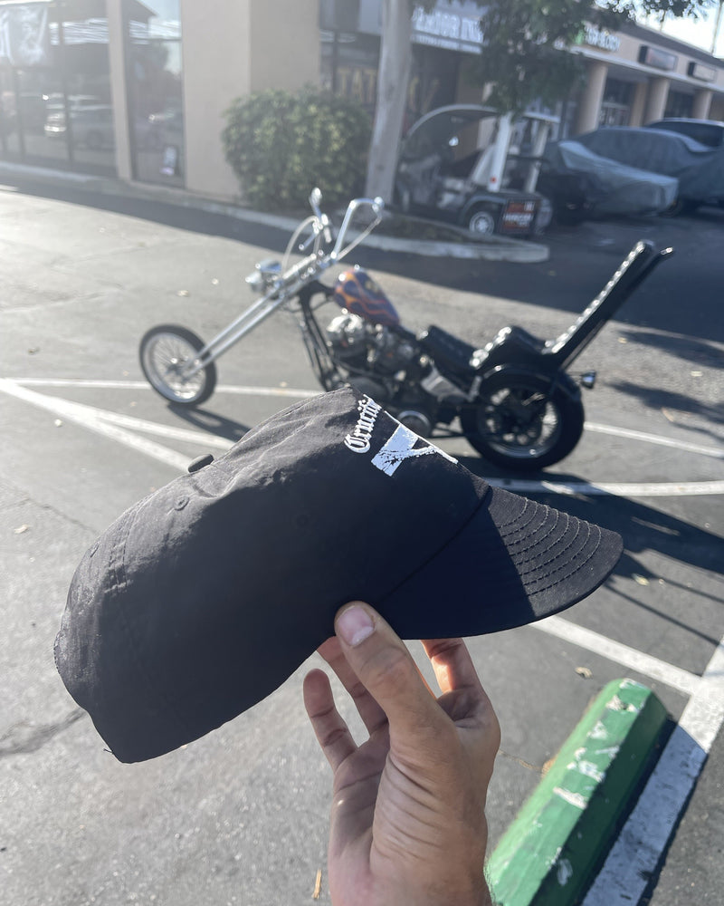 Hand bending the brim of the Crucified to Life hat beside a motorcycle