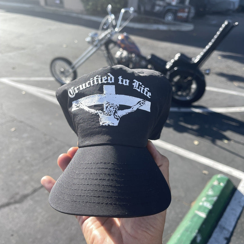 Crucified to Life hat held in front of a chopper motorcycle